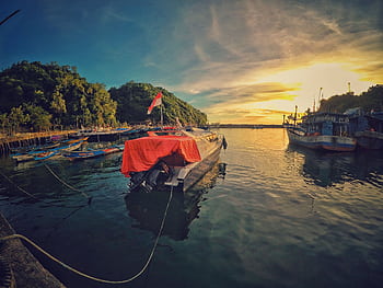 A stunning sunset view at Girisubo Harbor, Indonesia, with boats and lush hills. HD wallpaper