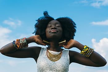 Portrait of a joyful African woman with afro hair, wearing colorful bracelets and gold earrings, enjoying the sunny day. HD wallpaper