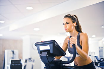 A determined woman using an elliptical machine indoors, focused and listening to music. HD wallpaper