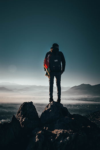 A lone hiker stands on a rocky peak, overlooking breathtaking mountains at sunrise in Afghanistan. HD phone wallpaper