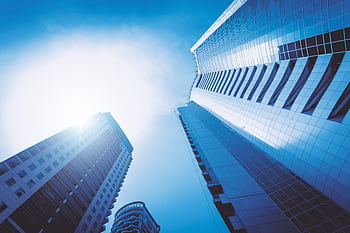 Low angle view of futuristic skyscrapers in a cityscape against a bright blue sky. HD wallpaper