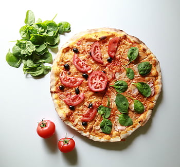 Freshly baked pizza topped with tomatoes, spinach, and olives, alongside fresh ingredients. HD wallpaper