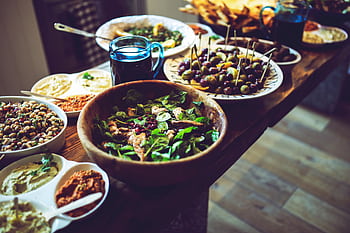 Mediterranean antipasti featuring olives, spinach salad, and dips on a rustic wooden table. HD wallpaper