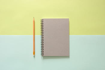 Flat lay of a spiral notebook and pencil on a pastel background, ideal for school and office themes. HD wallpaper