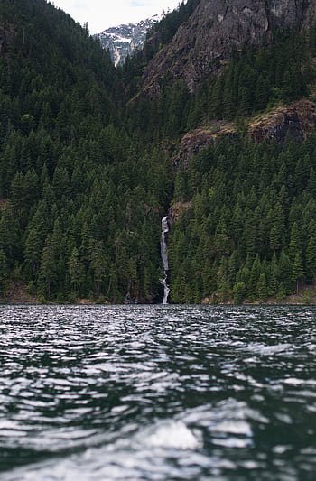 Tranquil lake with cascading waterfall in a lush green mountain forest setting. HD phone wallpaper