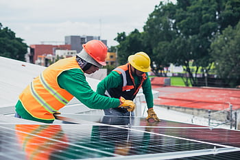Two workers installing rooftop solar panels safely equipped with PPE and tools. HD wallpaper