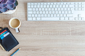 An organized workspace with a keyboard, coffee cup, wallet, and succulent plant on a wooden desk. HD wallpaper
