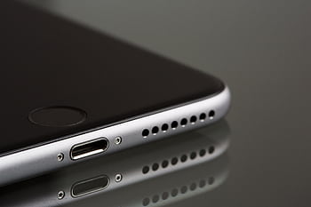 A sleek smart close-up highlighting its lightning connector and speaker, reflecting on a surface. HD wallpaper