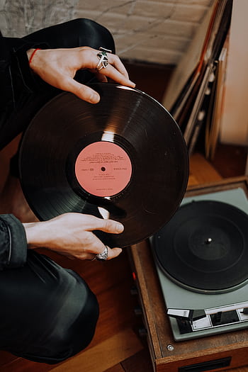 Close-up of hands with rings holding a classic vinyl record above a retro player. HD phone wallpaper