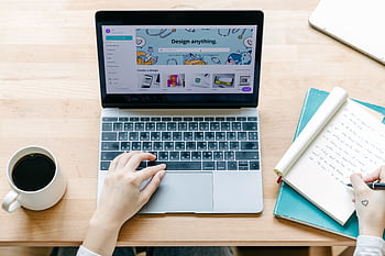 Top view of laptop with design app, coffee, and notepad on a wooden desk. HD wallpaper