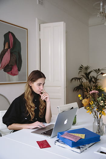 Woman working on a laptop at home, embracing digital nomad lifestyle. Modern workspace with plants. HD phone wallpaper