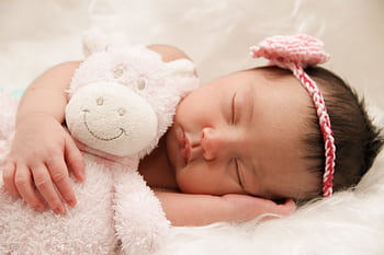 Adorable sleeping baby cuddling a plush toy, wearing a cute pink headband. HD wallpaper