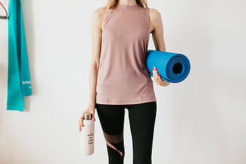 A woman in activewear holding a yoga mat and water bottle, ready for a workout. HD wallpaper