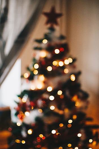 Blurred view of a Christmas tree adorned with twinkling lights and festive decorations, creating a warm holiday ambiance. HD phone wallpaper