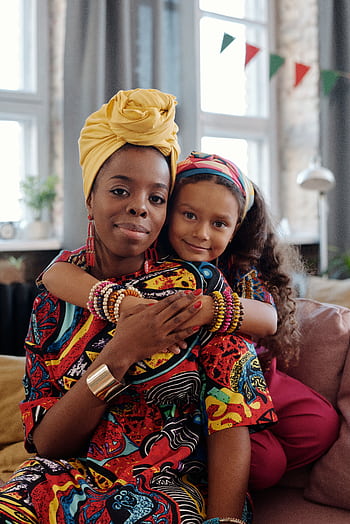 A loving embrace between a mother and daughter wearing vibrant traditional clothes indoors. HD phone wallpaper