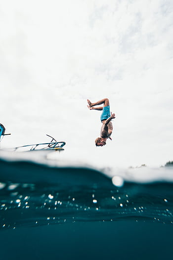 Man performing a backflip dive into the tropical ocean off a boat in Indonesia. HD phone wallpaper