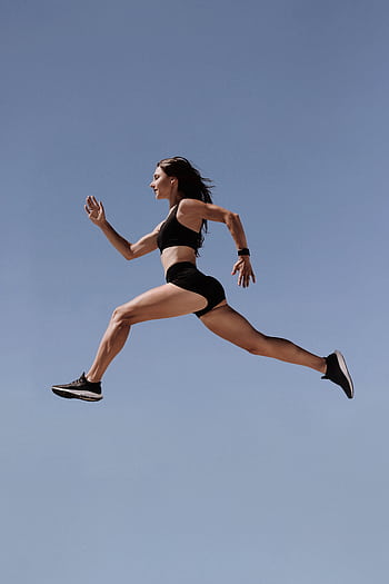 Energetic woman in athletic wear leaping against clear blue sky, symbolizing dom and fitness. HD phone wallpaper