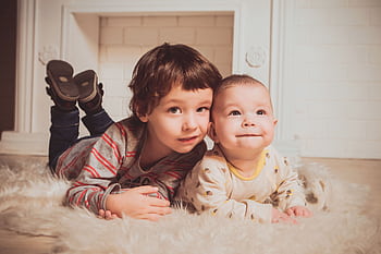 Two young siblings lying on a fluffy rug indoors, exemplifying warmth and family bonding. HD wallpaper