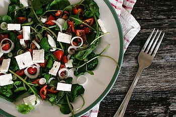 A vibrant and colorful spinach salad with feta cheese and tomatoes on a rustic table. HD wallpaper