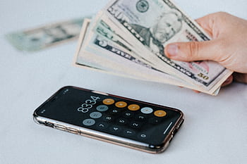 Hand holding dollar bills with smart calculator displaying 8334. HD wallpaper