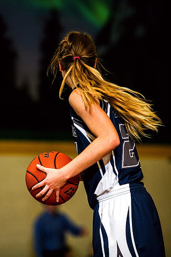 A young female basketball player holding a ball during an indoor game. HD phone wallpaper
