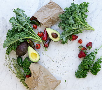 Top view of fresh avocados, kale, tomatoes, and peppers arranged on a marble surface. HD wallpaper