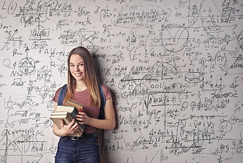 Young woman holding books standing in front of a chalkboard filled with mathematical formulas. HD wallpaper