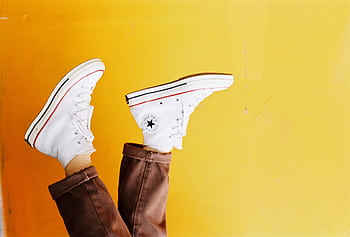 Upside down of white sneakers against a vibrant yellow background, showcasing trendy footwear style. HD wallpaper