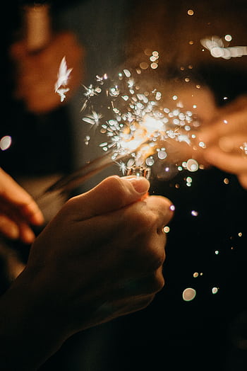 Close-up of hands holding sparklers during a lively New Year's Eve celebration. HD phone wallpaper