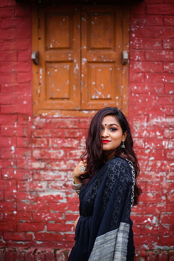 Charming woman in traditional attire posing against a rustic brick wall, showcasing elegance and cultural heritage. HD phone wallpaper