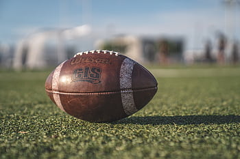 Close-up of a Wilson football on green grass in an outdoor sports setting, perfect for sports-themed visuals. HD wallpaper