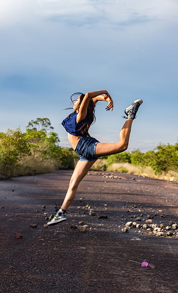 A woman performs a graceful dance leap on a sunlit outdoor path, showcasing fitness and flexibility. HD phone wallpaper