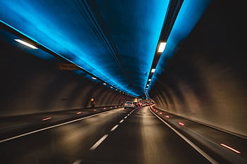 Long exposure capture of cars driving through a modern tunnel with blue lighting, showcasing speed and motion. HD wallpaper