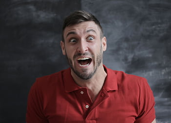 Expressive portrait of surprised man in red polo shirt with open mouth and wide eyes against a dark background. HD wallpaper
