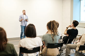 Man presenting with tablet to a small seated audience in a modern indoor setting. HD wallpaper