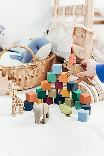 A child's hand arranges colorful wooden toys and animal figures on a playroom floor. HD phone wallpaper