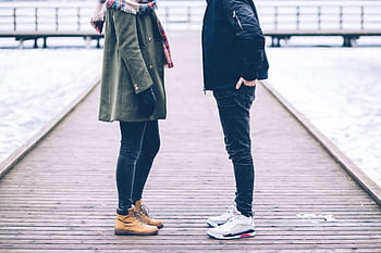 Couple standing on a snowy boardwalk in winter attire, showcasing fashion and romance. HD wallpaper