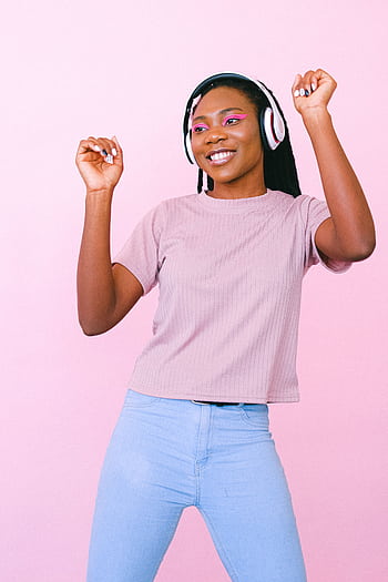 A young woman dances joyfully to music with heads on a pastel pink background. HD phone wallpaper