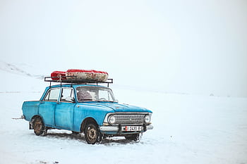 A vintage blue car with luggage on top amidst a snowy landscape in Kyrgyzstan. HD wallpaper