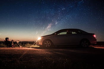A person relaxes by their car under a starry night sky, capturing tranquility. HD wallpaper