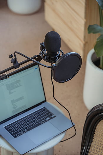 A modern podcast setup featuring a laptop and studio micro on a desk, ideal for digital media production. HD phone wallpaper