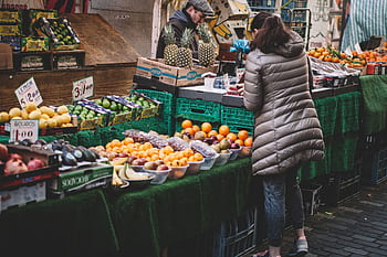Lively city market stall displaying diverse fresh fruits. A customer browses. HD wallpaper