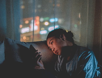 A woman looking at her mobile at night with city lights blurred in the background. HD wallpaper