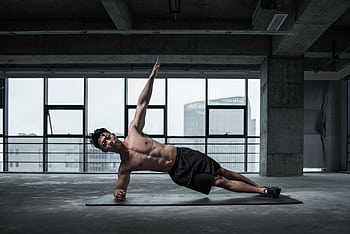 Fit man doing a side plank in an urban indoor gym, showcasing core strength and balance. HD wallpaper