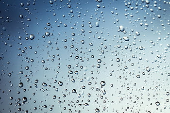 Crystal-clear water droplets on glass against a soft blue backdrop, capturing a rainy day essence. HD wallpaper