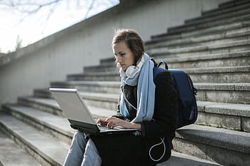 Woman using laptop on outdoor stairs, studying online with heads and backpack. HD wallpaper