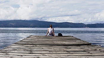 Woman sitting on a wooden pier, enjoying the serene lake view and mountains. HD wallpaper