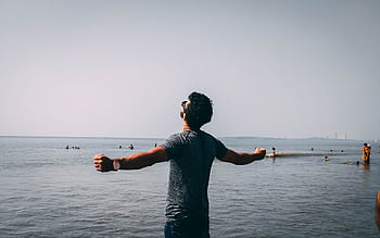 A man with open arms embracing dom on a sunny beach day, surrounded by people enjoying the water. HD wallpaper