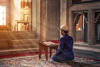 A young boy kneels in prayer inside a mosque with sunlight streaming through the window. HD wallpaper