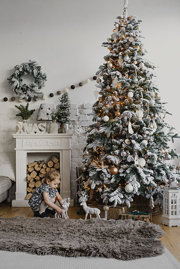 Charming indoor Christmas scene with a decorated tree and child by a cozy fireplace. HD phone wallpaper